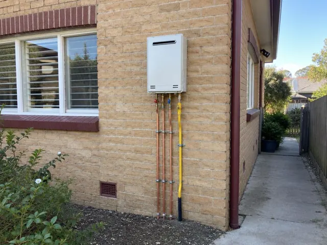 Wall-mounted hot water system with exposed pipework on a brick exterior wall in Cremorne